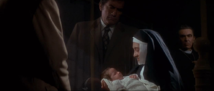 Robert Thorn (Gregory Peck) gazes on his accidental adoption while Father Spiletto (Martin Benson) approves.